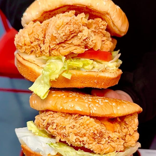 Two stacked Cluck & Crispy chicken sandwiches with lettuce, tomato, and sauce on sesame seed buns.
