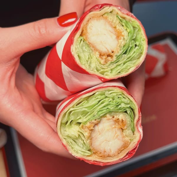 Hands holding two halves of a Cluck & Crispy chicken wrap with lettuce and sauce.