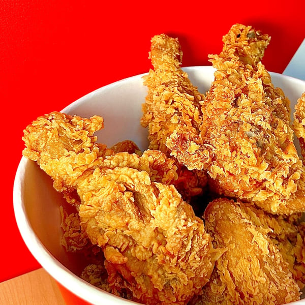 A bucket of Cluck & Crispy Chicken's golden-brown fried chicken pieces against a red background.