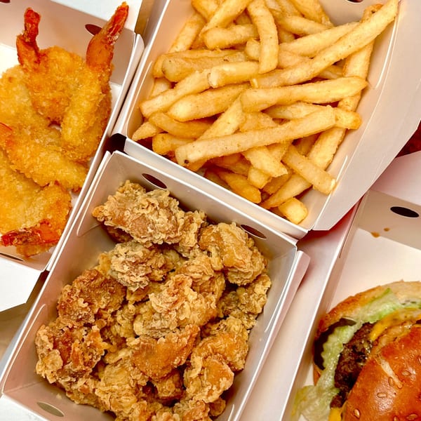 Cluck & Crispy fast-food meal with fried shrimp, french fries, crispy chicken, and a burger.