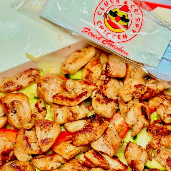 Grilled chicken pieces with lettuce, tomatoes, and cucumbers, with a Cluck & Crispy Chicken sauce packet.