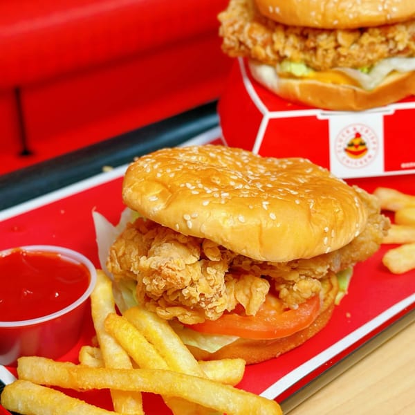 Cluck & Crispy Chicken sandwich with fries and ketchup on a red tray, with another sandwich in the background.