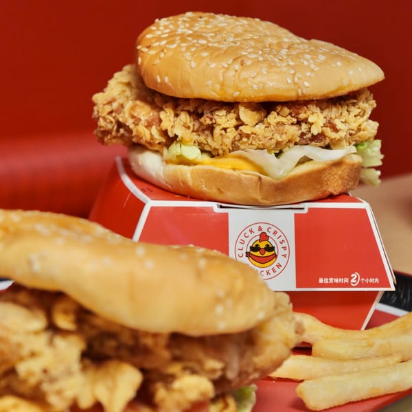 Two crispy chicken burgers with lettuce and cheese, one on a Cluck & Crispy box, with fries.